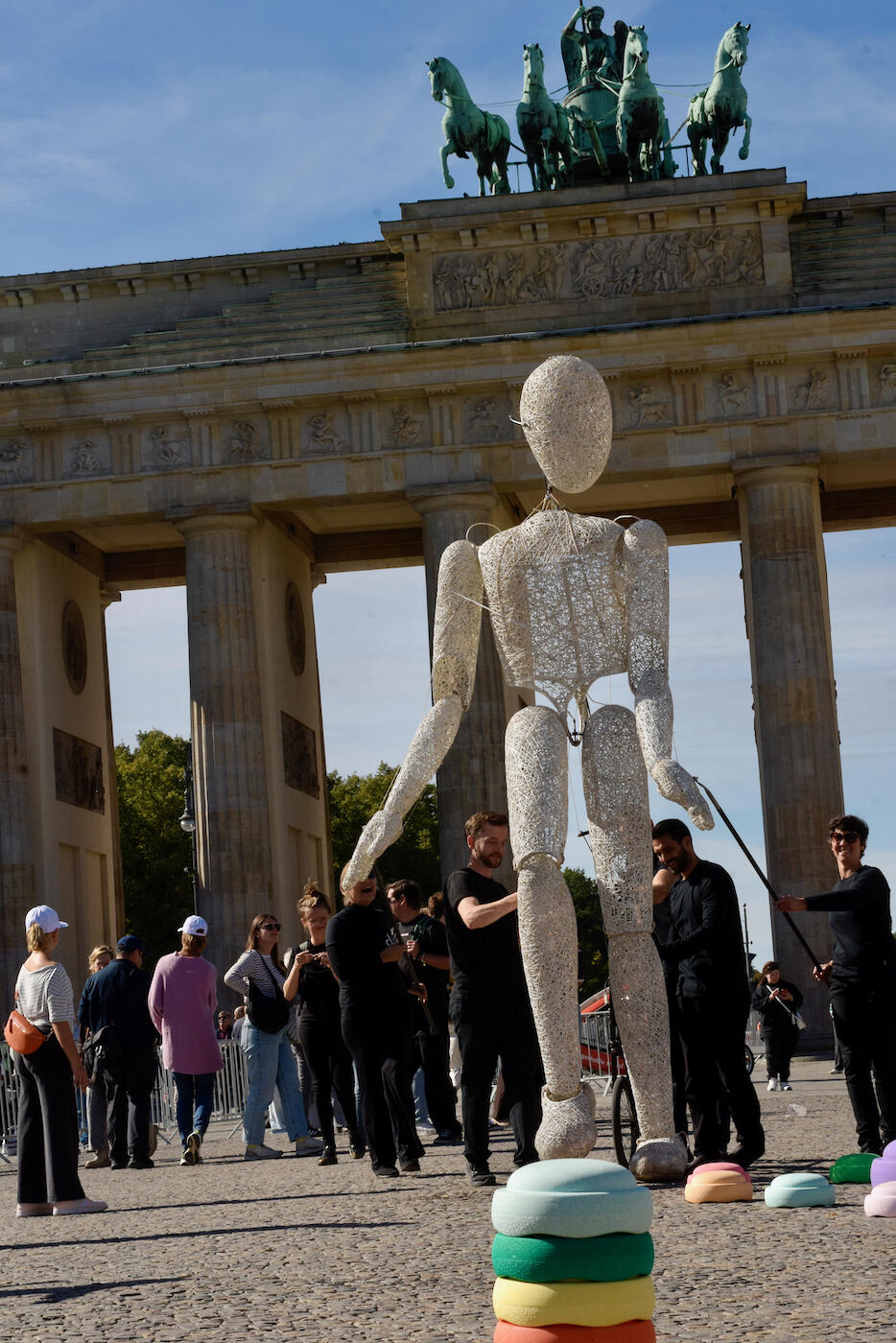 Große Drahtfigur vor dem Brandenburger Tor, umgeben von Besucherinnen und Besuchern